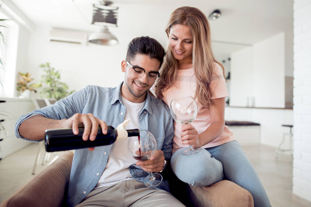 Amar pareja joven con copas de vino sentado en la sala de estar en casa
.  - Foto, imagen