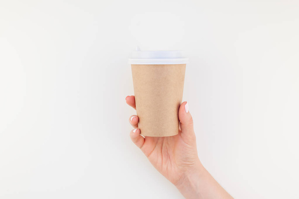 Creative mock up image of woman hand holding craft paper coffee cup with copy space isolated on white background in minimalism style. Template for feminine blog, social media - Photo, Image