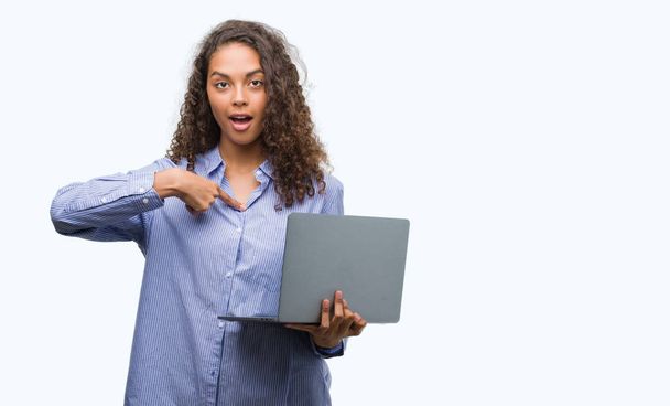Young hispanic woman holding computer laptop with surprise face pointing finger to himself - Zdjęcie, obraz