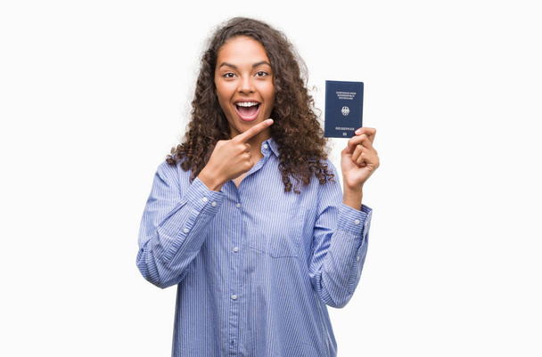 Jeune femme hispanique tenant passeport de l'Allemagne très heureux pointant avec la main et le doigt
 - Photo, image