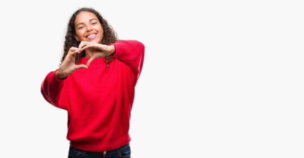 Jonge Spaanse vrouw dragen rode trui glimlachend in liefde met hartsymbool en vorm met de handen. Romantische concept. - Foto, afbeelding