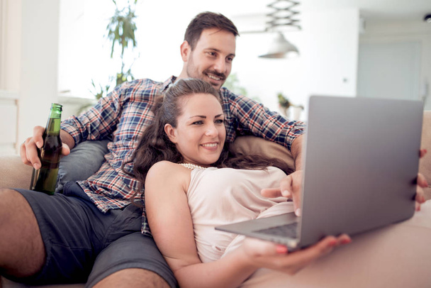 Young beautiful couple in love sitting on couch and using laptop. - Фото, зображення