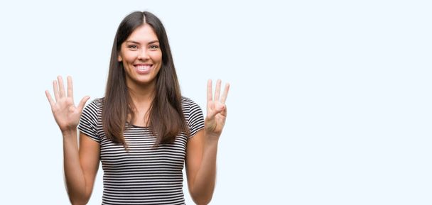 Joven mujer hispana hermosa mostrando y señalando hacia arriba con los dedos número ocho mientras sonríe confiado y feliz
. - Foto, Imagen