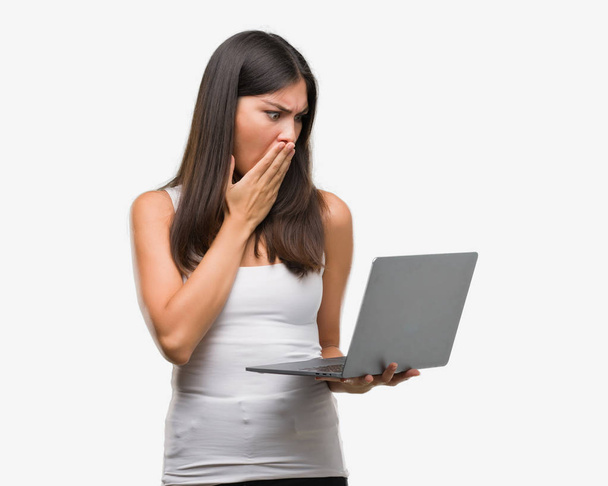 Young hispanic woman using computer laptop cover mouth with hand shocked with shame for mistake, expression of fear, scared in silence, secret concept - Foto, afbeelding