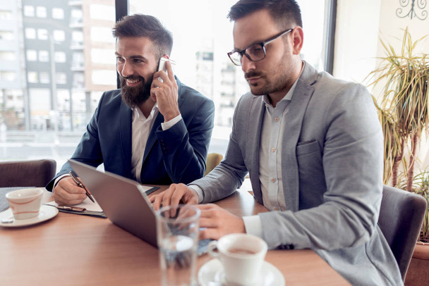 Deux hommes d'affaires confiants avec un sourire vérifier travailler sur ordinateur portable dans le bureau
. - Photo, image