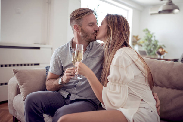 Hermosa pareja está bebiendo vino, hablando y sonriendo en el sofá en casa
. - Foto, Imagen
