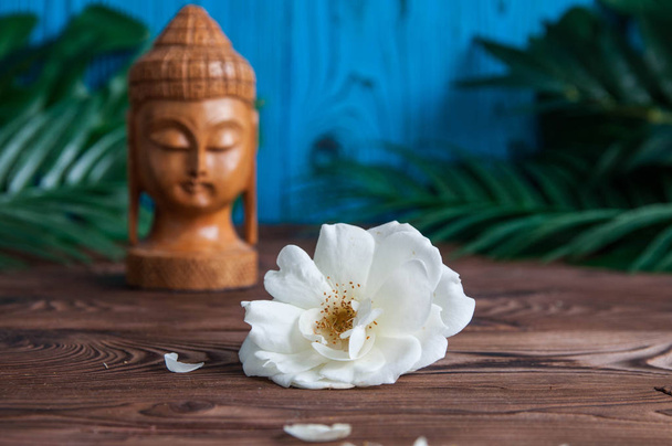 Άγαλμα του Βούδα με όμορφα άσπρα λουλούδια φρέσκα πράσινα φύλλα σε ξύλινο υπόβαθρο. Έννοια του αρμονία, ισορροπία και διαλογισμού, σπα, μασάζ, να χαλαρώσετε - Φωτογραφία, εικόνα