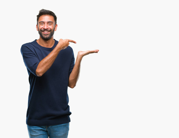 Adult hispanic man over isolated background amazed and smiling to the camera while presenting with hand and pointing with finger. - Photo, Image