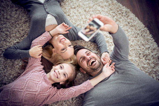 Top näkymä onnellinen perhe hymyilee kameralle, ota selfie ja makaa lattialla.Perhe, lapset ja kodin käsite
. - Valokuva, kuva