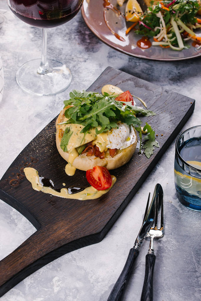 Φρέσκο κουλούρι σερβίρεται με μπέικον, αυγό Βενέδικτος υπό σάλτσα στην ξύλινη σανίδα - Φωτογραφία, εικόνα