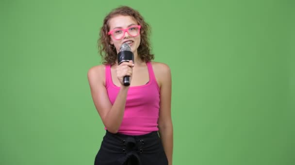 Young happy beautiful nerd woman presenting something with microphone - Imágenes, Vídeo