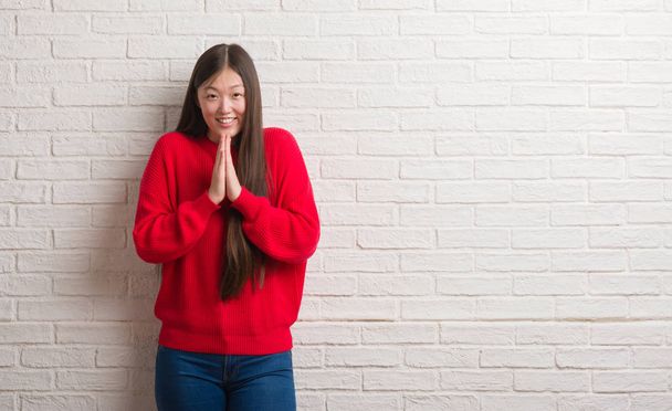 Mladá Číňanka cihlová zeď se modlí s rukama dohromady žádá o odpuštění usmívající se jistý. - Fotografie, Obrázek