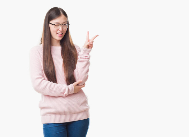 Jeune femme chinoise sur fond isolé portant des lunettes souriant avec un clin d'oeil heureux au visage de la caméra faisant signe de victoire. Numéro deux
. - Photo, image
