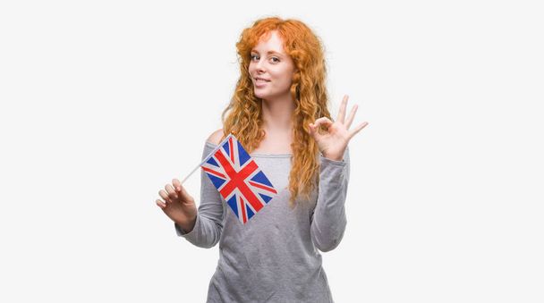 Jovem ruiva segurando bandeira do Reino Unido fazendo sinal ok com os dedos, excelente símbolo
 - Foto, Imagem