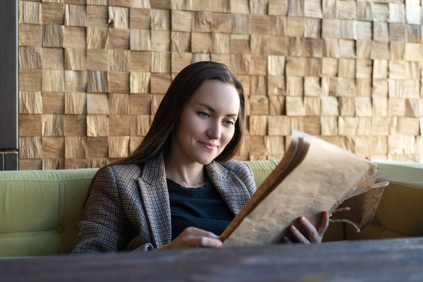 Una giovane donna seduta in un ristorante con un menu in mano fa una scelta di piatti
. - Foto, immagini