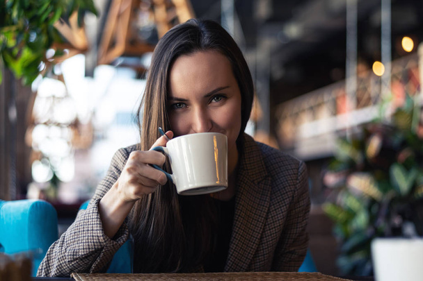 Портрет молодой деловой женщины, пьющей чай из чашки крупным планом с размытым ресторанным фоном
. - Фото, изображение
