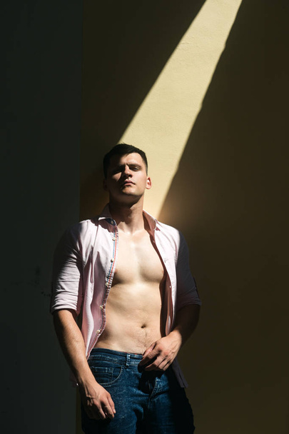 Man in open shirt show sexy torso. Man model with serious face look on sunny wall - Valokuva, kuva