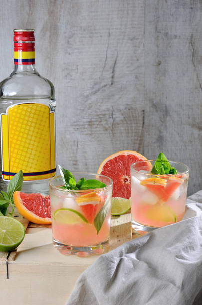 Cocktail van London dry gin met SAP uit geperst rode grapefruit en bladeren van delicate basilicum, citroen, limoen segmenten en gekoeld ijsblokjes. - Foto, afbeelding