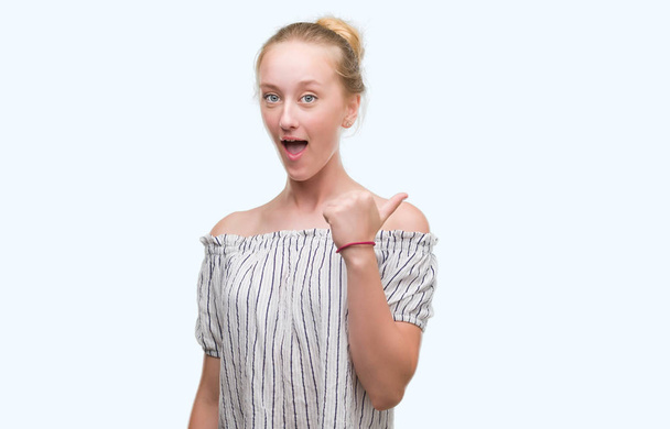 Rubia adolescente mujer usando un moño señalando y mostrando con el pulgar hacia arriba a un lado con la cara feliz sonriendo
 - Foto, imagen