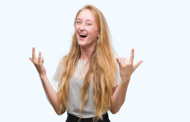 Blondi teini-ikäinen nainen yllään myyrät paita huutaa hullu ilme tekee rock symboli kädet ylhäällä. Musiikkitähti. Raskas käsite
. - Valokuva, kuva