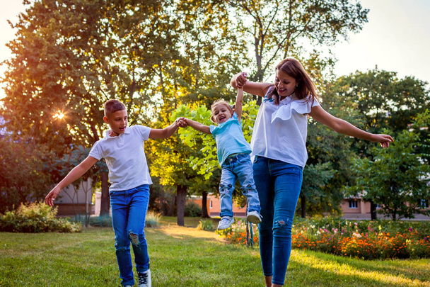 Ευτυχισμένος οικογενειακές δαπάνες το χρόνο τους σε εξωτερικούς χώρους παίζοντας στο πάρκο. Μαμά διασκεδάζοντας με δύο παιδιά αγόρι και κορίτσι. Εμετό νήπιο. Οικογενειακές αξίες - Φωτογραφία, εικόνα