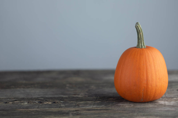 One orange pumpkin on old wooden table over gray background, Halloween concept - 写真・画像
