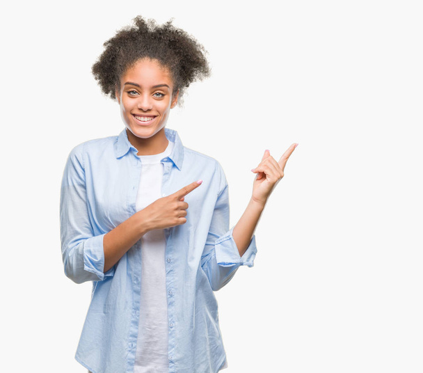 Młody afro american kobieta na białym tle uśmiechając się i patrząc na kamery, wskazując z dwóch rąk i palców na bok. - Zdjęcie, obraz