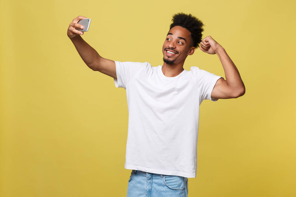 jonge afro Amerikaanse zwarte man die lacht gelukkig nemen selfie zelf portret foto met mobiele telefoon op zoek met opgewonden leuke poseren cool geïsoleerd op gele achtergrond in communicatietechnologie - Foto, afbeelding