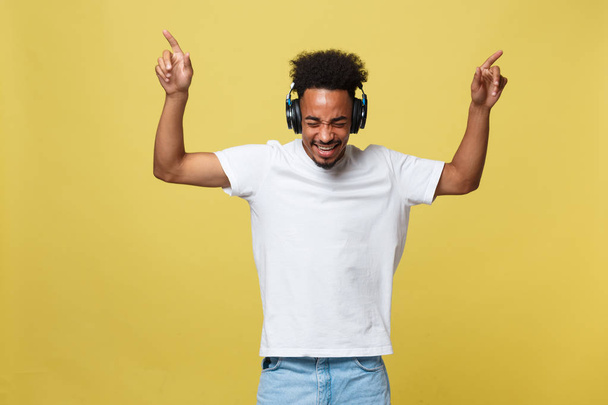 Młody African American man noszenia słuchawek i cieszyć się muzyka nad złoto żółte tło - Zdjęcie, obraz