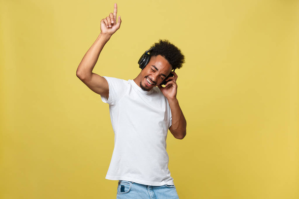 junger afrikanisch-amerikanischer Mann trägt Kopfhörer und genießt Musik über gelbgoldenem Hintergrund. - Foto, Bild