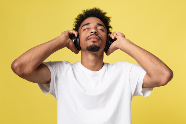 Fiatal afroamerikai férfi viselt fejhallgató, és élvezze a zene sárga arany háttér - Fotó, kép