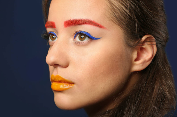Young woman with dyed eyebrows and creative makeup on dark background, closeup - Photo, Image