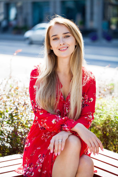 Portrait close up of young beautiful happy blonde woman in red dress, summer street outdoors - Photo, Image