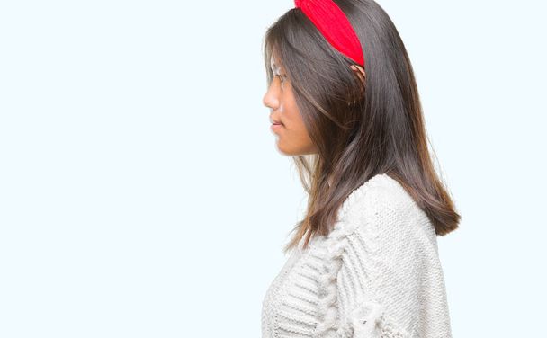 Jonge Aziatische vrouw dragen winter trui over geïsoleerde achtergrond op zoek naar kant, ontspannen profiel pose met natuurlijke gezicht met vertrouwen glimlach. - Foto, afbeelding