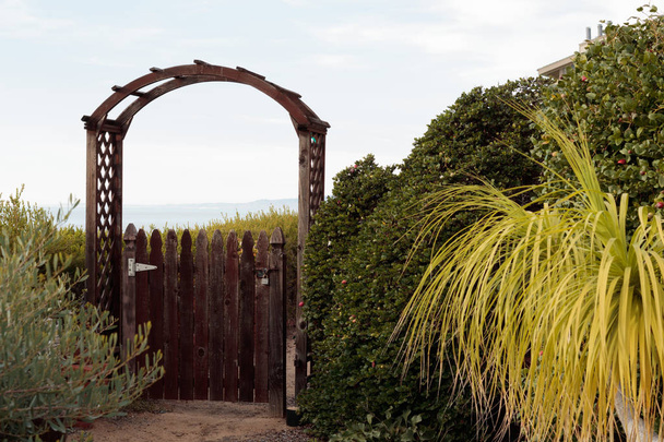 Puerta de madera natural se abre a la vista lejana de oportunidad o misterio, un camino arenoso a la puerta está rodeado de follaje verde
 - Foto, imagen