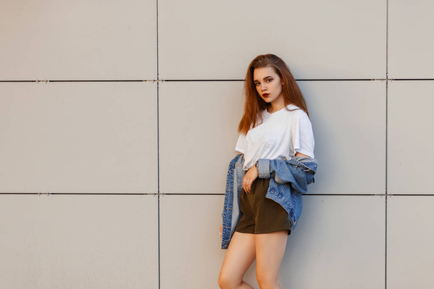 Fashionable beautiful young stylish woman model in vintage jeans clothes in a gray T-shirt with shorts near a modern wall - Fotografie, Obrázek