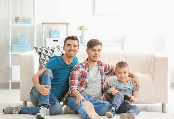 Male gay couple and adopted boy with laptop on floor at home - Foto, Bild