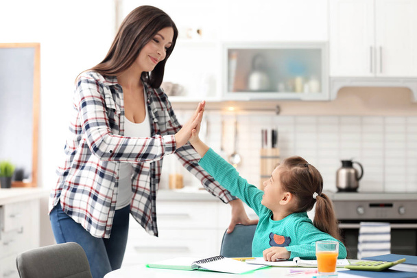Cute little girl doing homework with mother in kitchen - Photo, Image