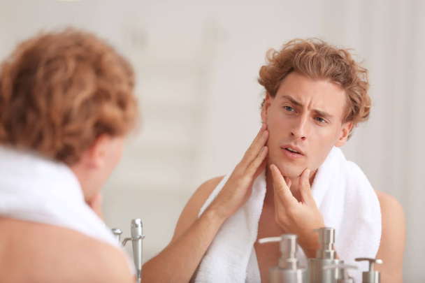Young man looking in mirror after shaving at home - Фото, изображение