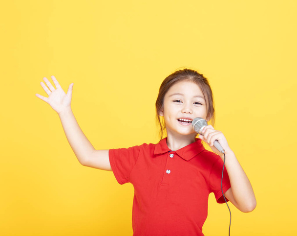 happy little girl singing on yellow background - Photo, Image