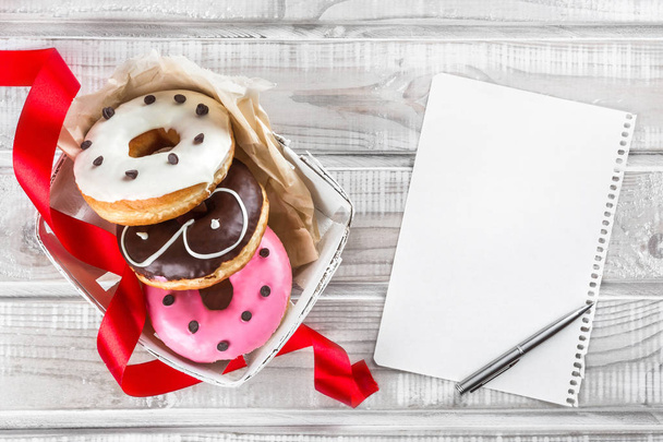 Uma caixa de donuts doces, um presente para o querido, uma vista superior, uma folha branca para uma mensagem de saudação
 - Foto, Imagem