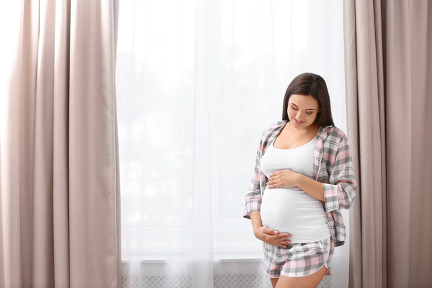 Giovane bella donna incinta vicino alla finestra a casa
 - Foto, immagini