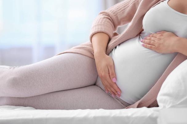 Jeune femme enceinte couchée sur le lit et touchant son ventre à la maison, gros plan
 - Photo, image