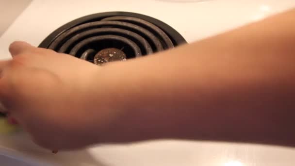 Een hand neemt een groene en gele borstelig spons en veegt omhoog tomaat vlekken vanaf de bovenkant van een fornuis  - Video
