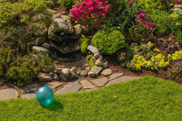 春の日差しで明るいターコイズ ブルー子供おもちゃボールと裏庭の庭の石造りの噴水の設計 - 写真・画像