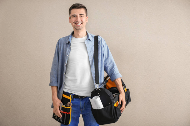 Young plumber with tool belt and bag on light background - Фото, зображення