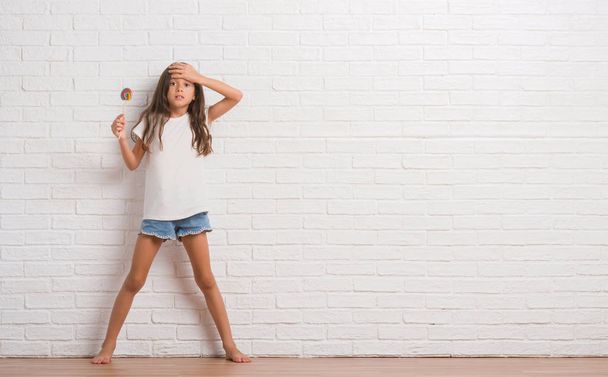 Молода іспаномовна дитина над білою цегляною стіною їсть цукерки льодяника вдома, напружені рукою на голові, шоковані соромом і несподіваним обличчям, розлючені і розчаровані. Страх і засмучення за помилку
. - Фото, зображення