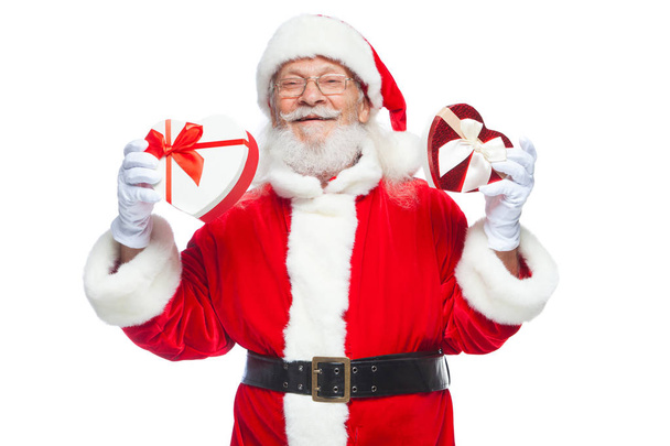 Navidad. Santa Claus sonriente con guantes blancos sostiene dos cajas de regalo en forma de corazón rojo y blanco con una cinta. El concepto de regalos generosos. Aislado sobre fondo blanco
. - Foto, Imagen