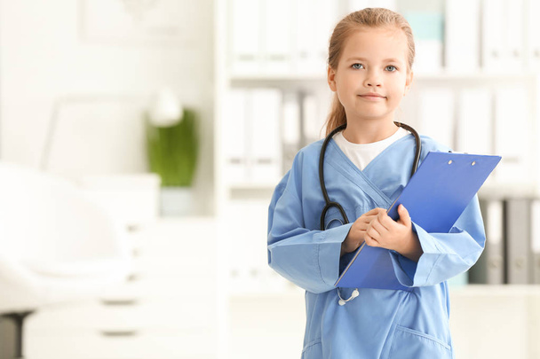 Cute little girl in doctor uniform with clipboard in hospital - Photo, Image