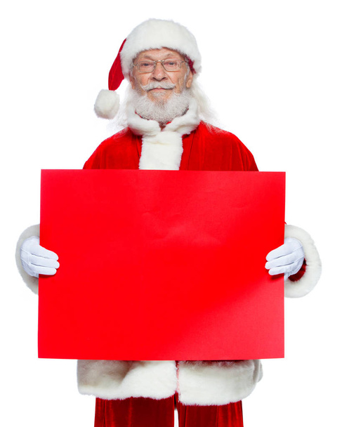 Christmas. The kind Santa Claus in white gloves holds an empty cardboard of red color. Place for advertising, for text, empty space. Copy-paste. Isolated on white background. - Photo, Image